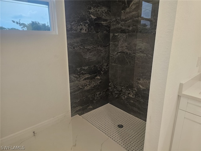 bathroom featuring a tile shower, vanity, and baseboards