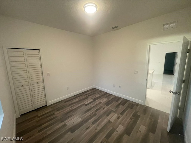 unfurnished bedroom with dark wood-style floors, a closet, visible vents, and baseboards