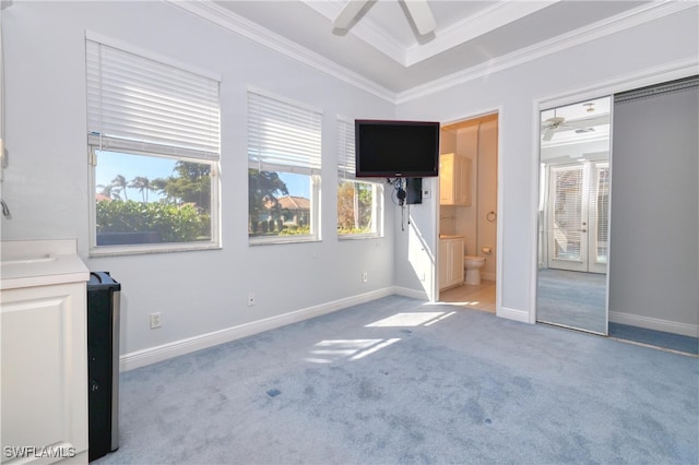 unfurnished bedroom with crown molding, ensuite bath, a tray ceiling, carpet flooring, and ceiling fan