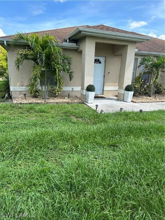 212 Paxton St, Lehigh Acres, FL 33974 - entrance to property featuring a yard, stucco siding, and roof with shingles