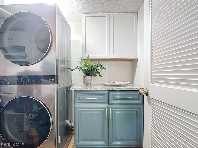 laundry area featuring stacked washer / dryer, cabinets, and a textured ceiling