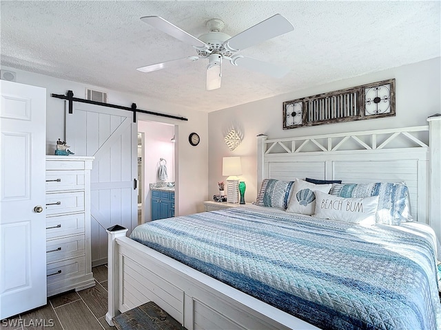 bedroom featuring a textured ceiling, ceiling fan, a barn door, and ensuite bathroom