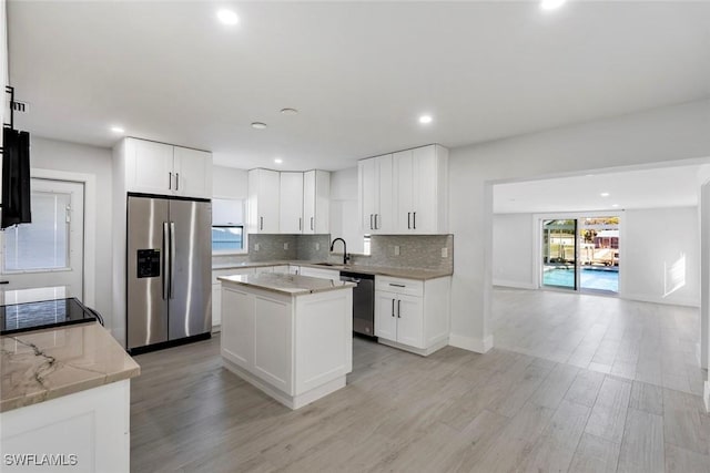 kitchen featuring a center island, white cabinets, sink, appliances with stainless steel finishes, and light stone counters