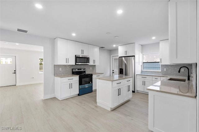 kitchen featuring appliances with stainless steel finishes, white cabinetry, a kitchen island, and sink