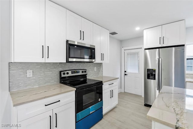 kitchen with light stone counters, backsplash, light hardwood / wood-style floors, white cabinets, and appliances with stainless steel finishes