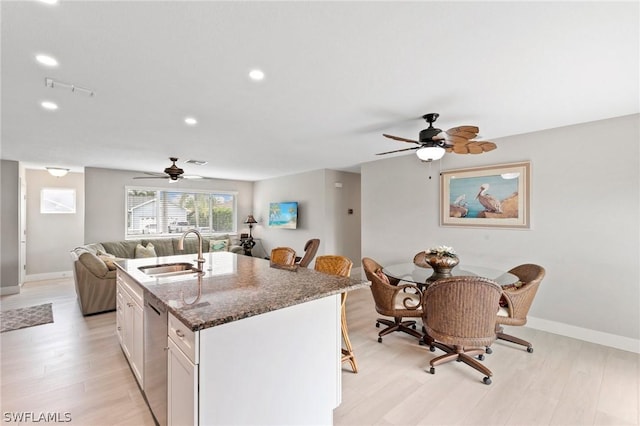 kitchen featuring sink, dark stone countertops, white cabinets, a kitchen bar, and stainless steel dishwasher