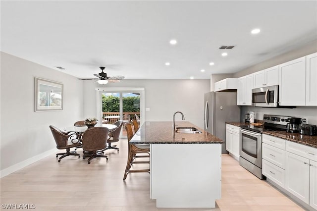 kitchen featuring a kitchen island with sink, a breakfast bar area, stainless steel appliances, and dark stone counters