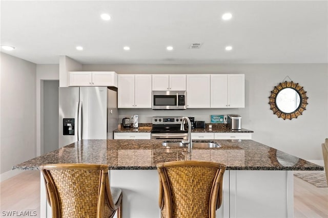 kitchen featuring stainless steel appliances, an island with sink, dark stone countertops, and white cabinets