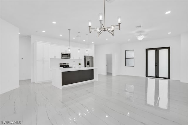 kitchen with appliances with stainless steel finishes, white cabinets, ceiling fan with notable chandelier, decorative light fixtures, and a kitchen island with sink