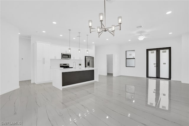 kitchen with pendant lighting, a kitchen island with sink, ceiling fan with notable chandelier, white cabinetry, and stainless steel appliances