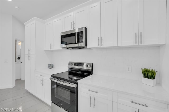 kitchen featuring light stone countertops, stainless steel appliances, white cabinets, and decorative backsplash