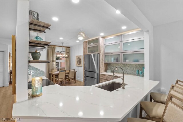 kitchen featuring sink, kitchen peninsula, stainless steel refrigerator, and tasteful backsplash