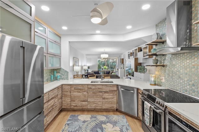 kitchen with wall chimney range hood, ceiling fan, stainless steel appliances, light hardwood / wood-style floors, and decorative backsplash