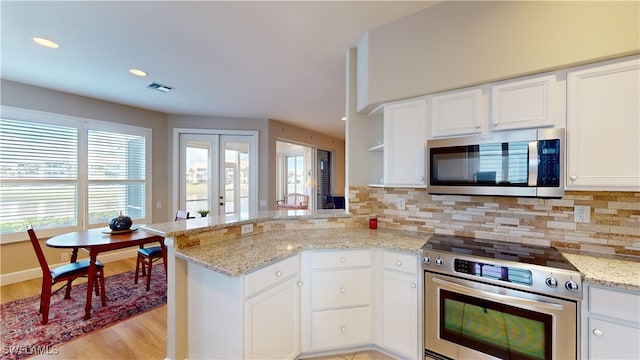 kitchen with white cabinetry, light stone countertops, light hardwood / wood-style floors, kitchen peninsula, and stainless steel appliances