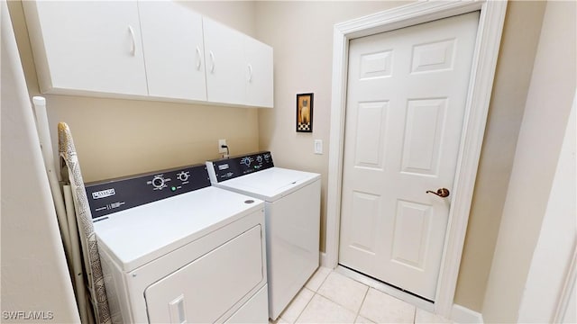 clothes washing area with cabinets, light tile patterned floors, and washer and dryer