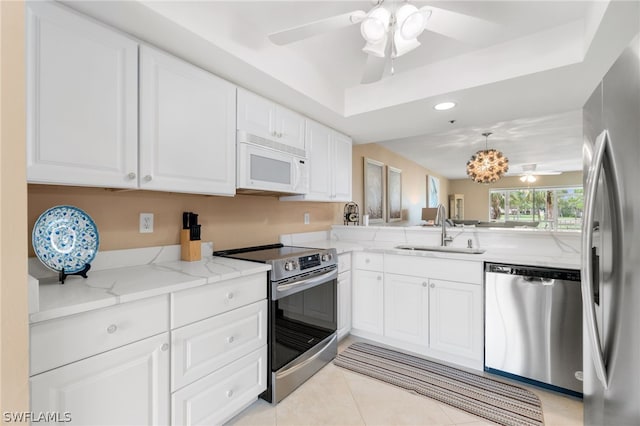 kitchen featuring stainless steel appliances, white cabinets, sink, ceiling fan, and a tray ceiling