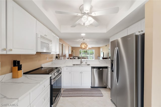 kitchen with light tile patterned flooring, white cabinets, ceiling fan with notable chandelier, stainless steel appliances, and a raised ceiling