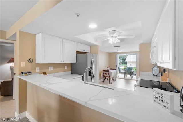 kitchen featuring a peninsula, light stone counters, white cabinets, and freestanding refrigerator