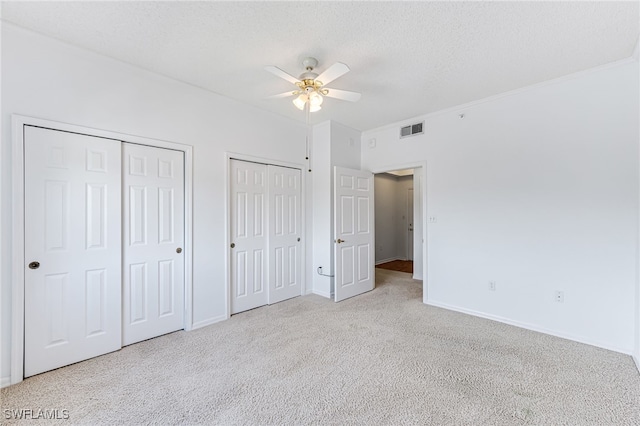 unfurnished bedroom featuring a textured ceiling, light carpet, visible vents, baseboards, and two closets