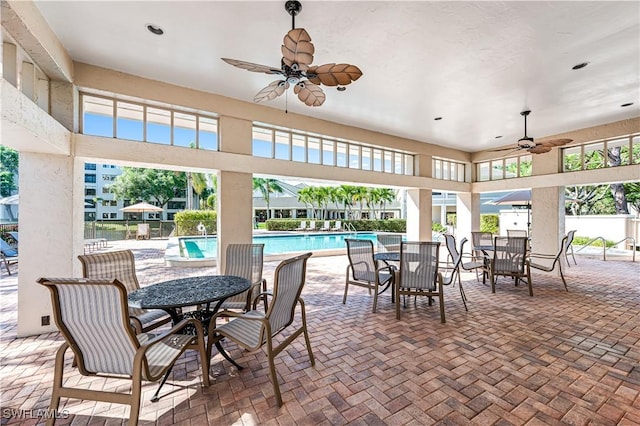 view of patio featuring a community pool, fence, outdoor dining area, and a ceiling fan