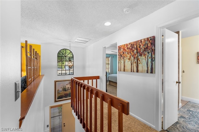 corridor featuring a chandelier, a textured ceiling, and carpet