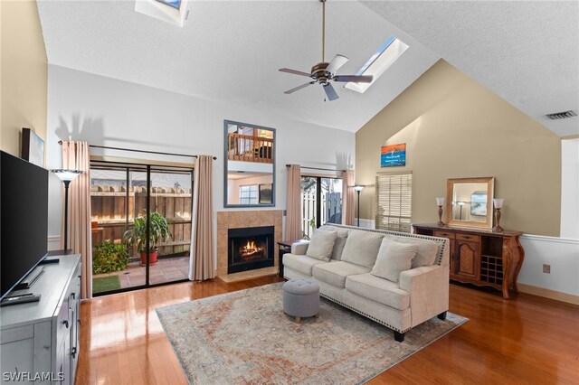 living room featuring hardwood / wood-style floors, a tiled fireplace, high vaulted ceiling, and a skylight