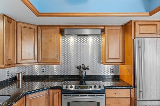 kitchen featuring wall chimney exhaust hood, decorative backsplash, dark stone counters, and appliances with stainless steel finishes