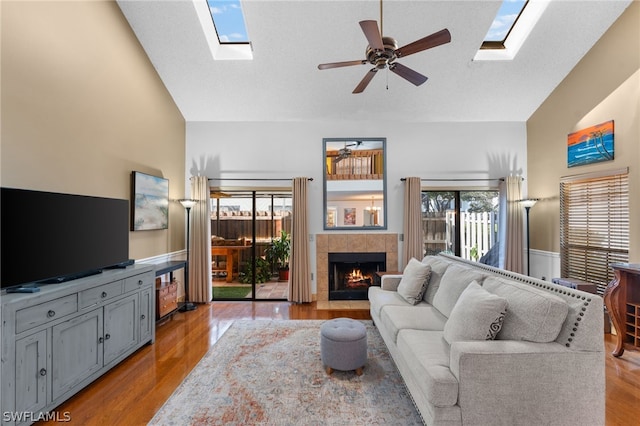 living room featuring high vaulted ceiling, a skylight, a tiled fireplace, and light wood-type flooring