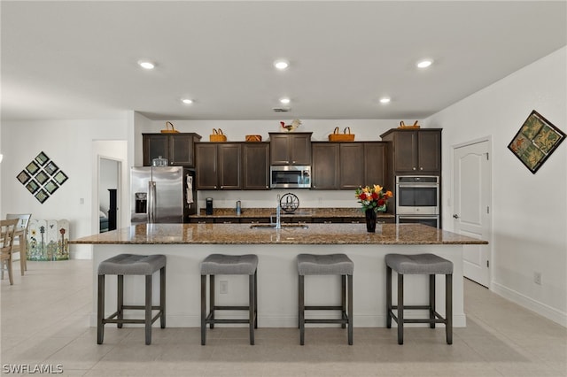 kitchen with a breakfast bar area, an island with sink, stainless steel appliances, dark brown cabinetry, and sink