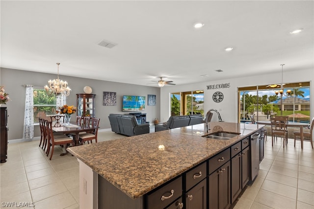 kitchen with dark stone countertops, light tile patterned floors, a kitchen island with sink, pendant lighting, and sink