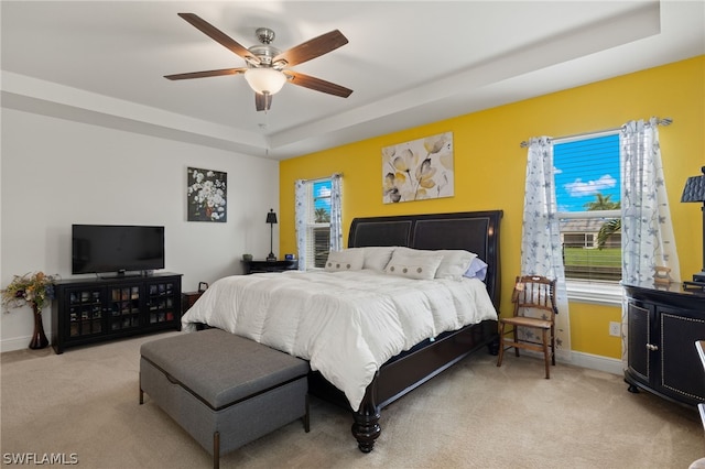 carpeted bedroom with ceiling fan and a raised ceiling