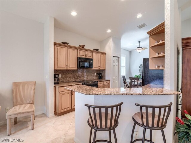 kitchen with black appliances, a kitchen bar, light tile patterned floors, and backsplash