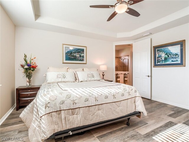 bedroom with hardwood / wood-style flooring, a raised ceiling, and ceiling fan