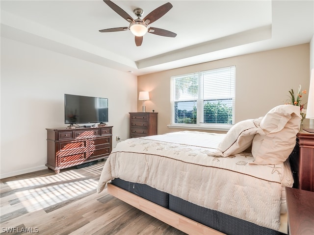 bedroom featuring light wood-type flooring, ceiling fan, and a raised ceiling