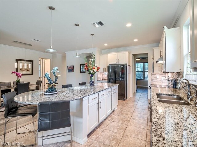 kitchen featuring tasteful backsplash, sink, a kitchen island, light stone countertops, and black fridge