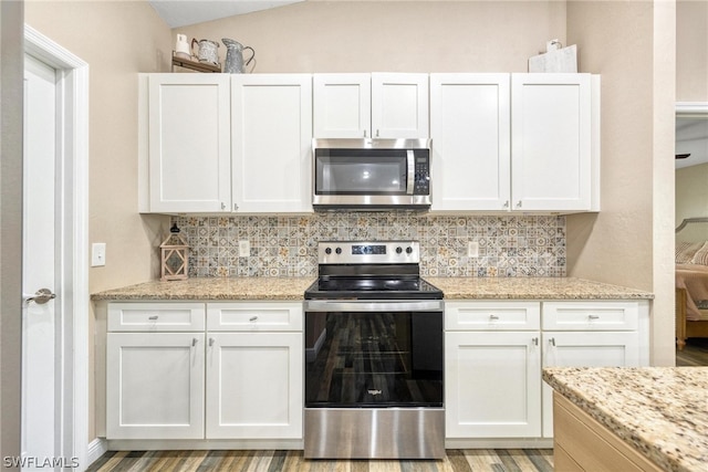 kitchen with vaulted ceiling, white cabinetry, backsplash, and stainless steel appliances