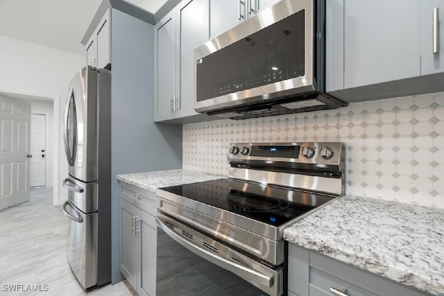 kitchen featuring tasteful backsplash, light stone countertops, appliances with stainless steel finishes, and gray cabinets