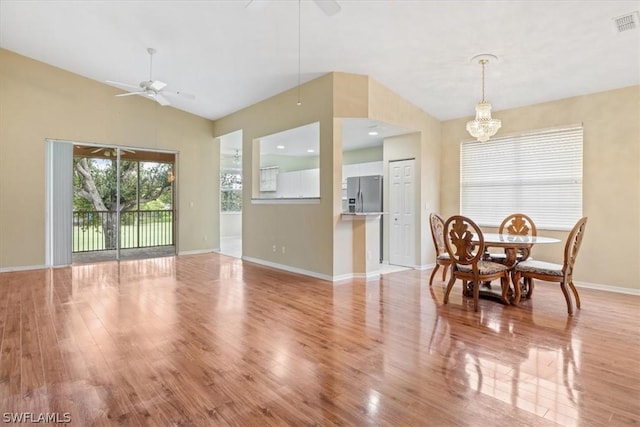 dining space with ceiling fan with notable chandelier, light wood-type flooring, and vaulted ceiling