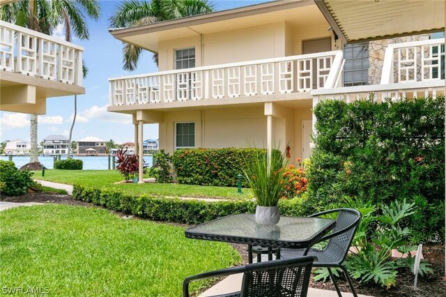 rear view of house with a balcony, a water view, and a yard