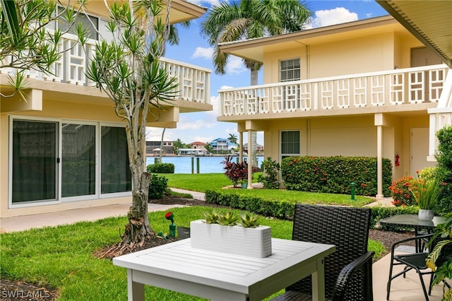 back of house featuring a balcony, a water view, and a yard