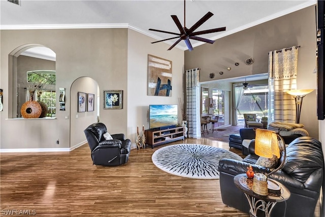 living room featuring crown molding, ceiling fan, wood-type flooring, and a towering ceiling