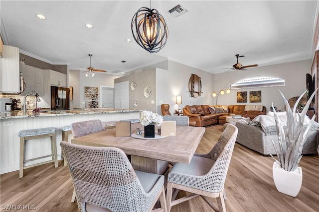 dining space with crown molding, ceiling fan with notable chandelier, and light hardwood / wood-style floors