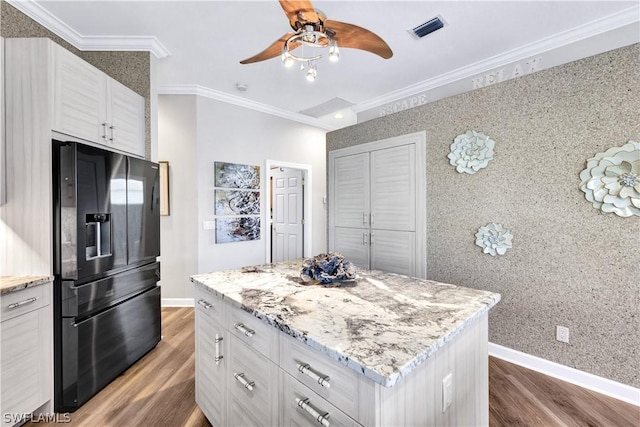 kitchen with black fridge, crown molding, light stone counters, and white cabinets