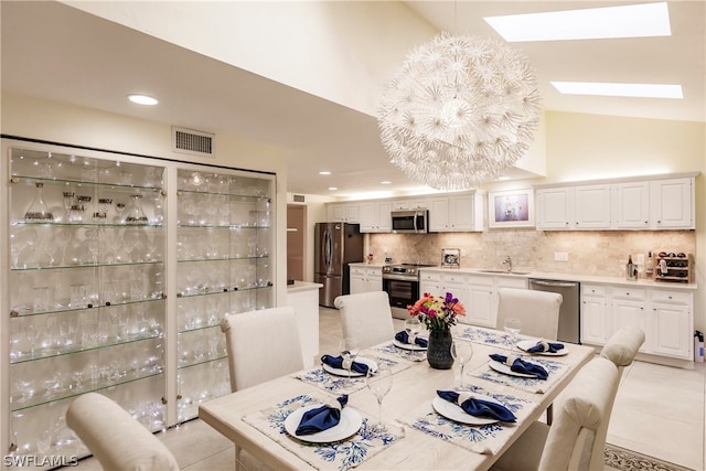 tiled dining area featuring a skylight, sink, and high vaulted ceiling