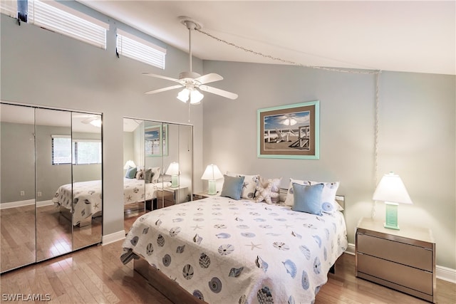 bedroom featuring two closets, high vaulted ceiling, ceiling fan, and hardwood / wood-style floors