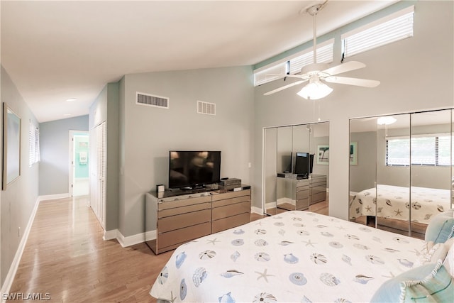 bedroom with multiple closets, light hardwood / wood-style floors, high vaulted ceiling, and ceiling fan