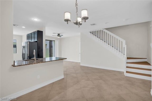 kitchen featuring decorative light fixtures, dark stone countertops, stainless steel fridge, kitchen peninsula, and ceiling fan with notable chandelier