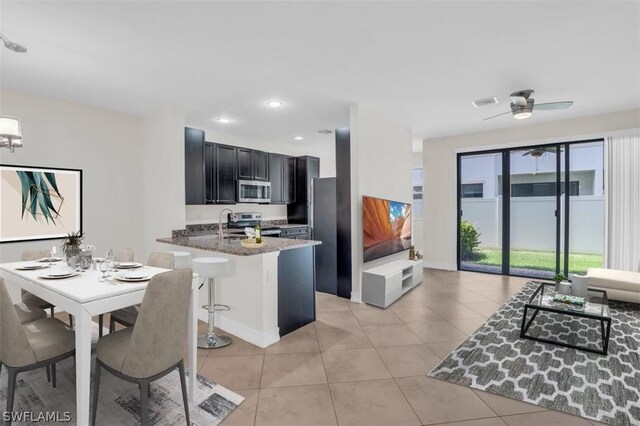 kitchen with ceiling fan, stainless steel appliances, stone counters, a kitchen bar, and kitchen peninsula