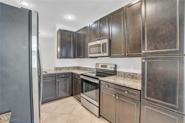 kitchen with light stone countertops, appliances with stainless steel finishes, light tile patterned floors, and dark brown cabinetry