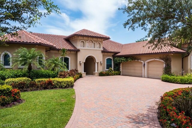 20180 Riverbrooke Run, Estero, FL 33928 - mediterranean / spanish-style house featuring decorative driveway, an attached garage, stucco siding, a front lawn, and a tiled roof